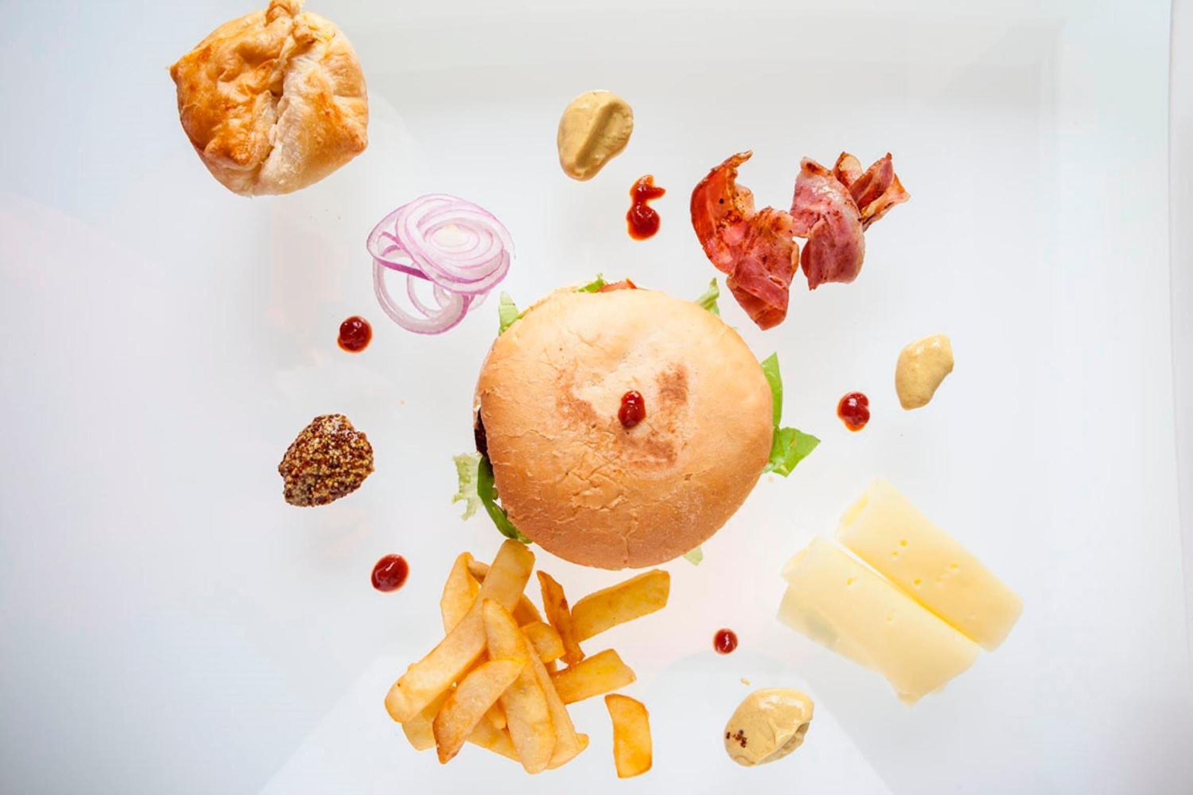 A burger with fries, cheese, and condiments on a white plate.