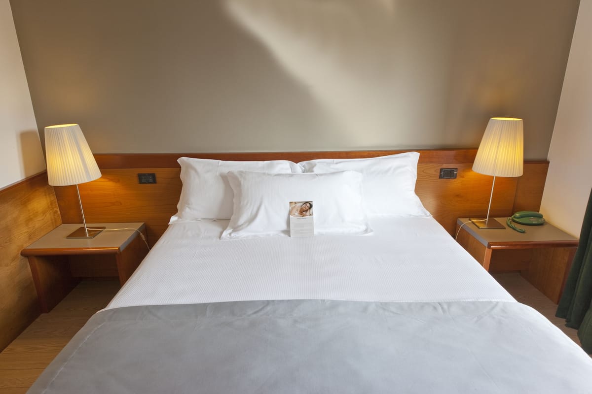 A neatly made bed with white linens, two bedside lamps, and a small bedside table with a green telephone.