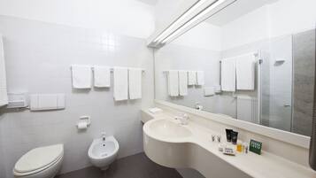 Une salle de bain moderne équipée de toilettes, d’un bidet et d’un lavabo. Plusieurs serviettes blanches sont accrochées au mur, et un grand miroir se trouve au-dessus du lavabo.