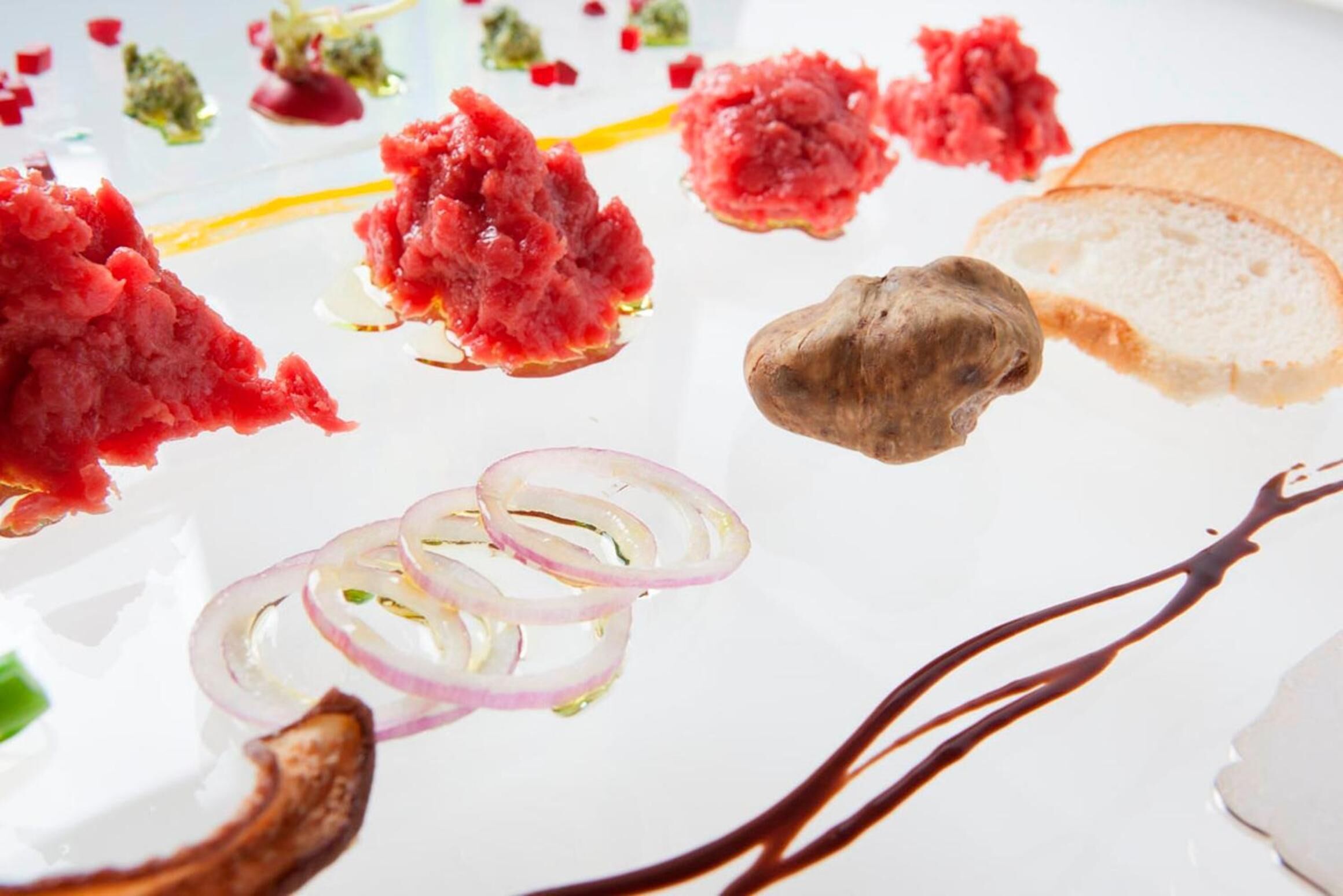 A white plate with various food items including red meat, sliced onions, and a piece of ginger.
