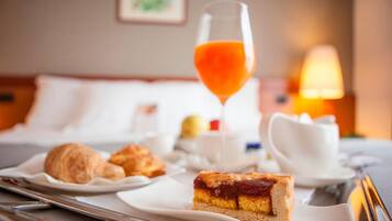Una mesa con cruasanes, una rebanada de pastel, un vaso de jugo de naranja y una tetera.