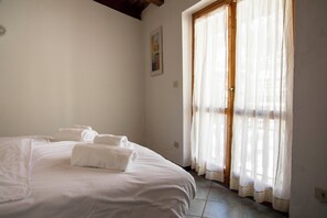 A bedroom with a bed, towels, a window with curtains, and a painting on the wall. - Residence Nube D'argento (Sestriere)