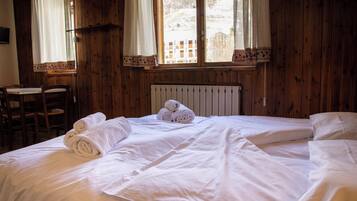 A wooden room with a bed, two chairs, a table, and a window with a view of a snowy landscape.