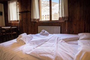 A wooden room with a bed, two chairs, a table, and a window with a view of a snowy landscape.