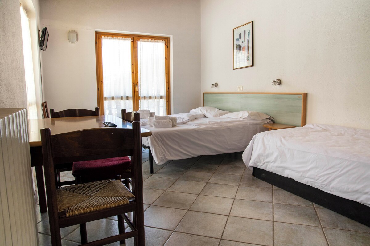 A hotel room with a bed, a chair, a table, and a window with curtains.