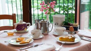 Une table de petit-déjeuner avec des tasses à thé et à café, une théière, un pichet, une assiette avec des toasts et de la confiture, et une part de tarte.
