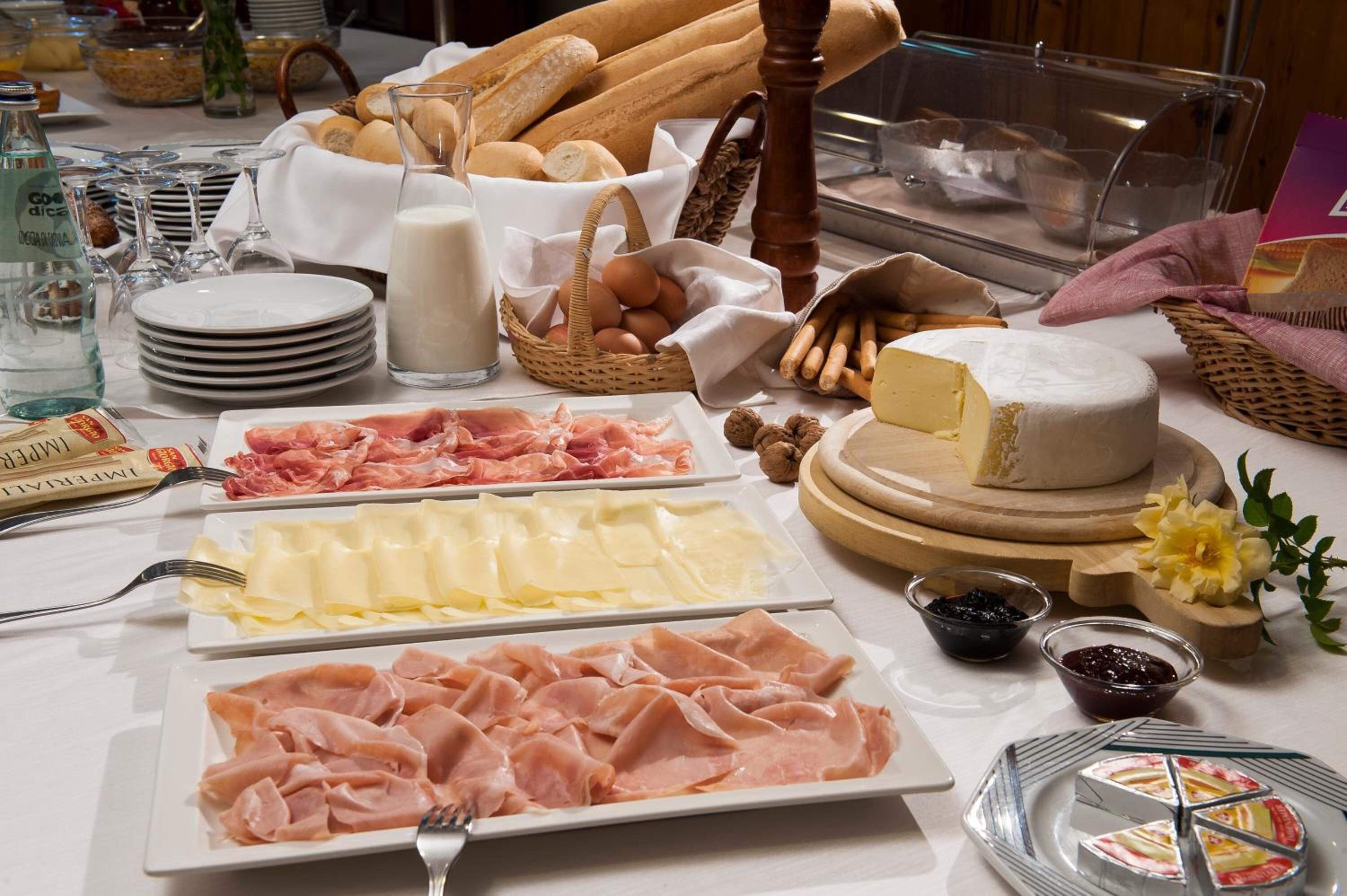 A breakfast buffet with various cheeses, meats, bread, and beverages.