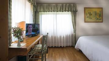 Una camera d'albergo con una scrivania in legno, una televisione, una sedia, un letto e un quadro appeso al muro.