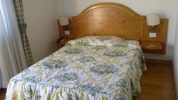 A single bed with a floral bedspread, wooden headboard, two wall-mounted lamps, and a small wooden nightstand.