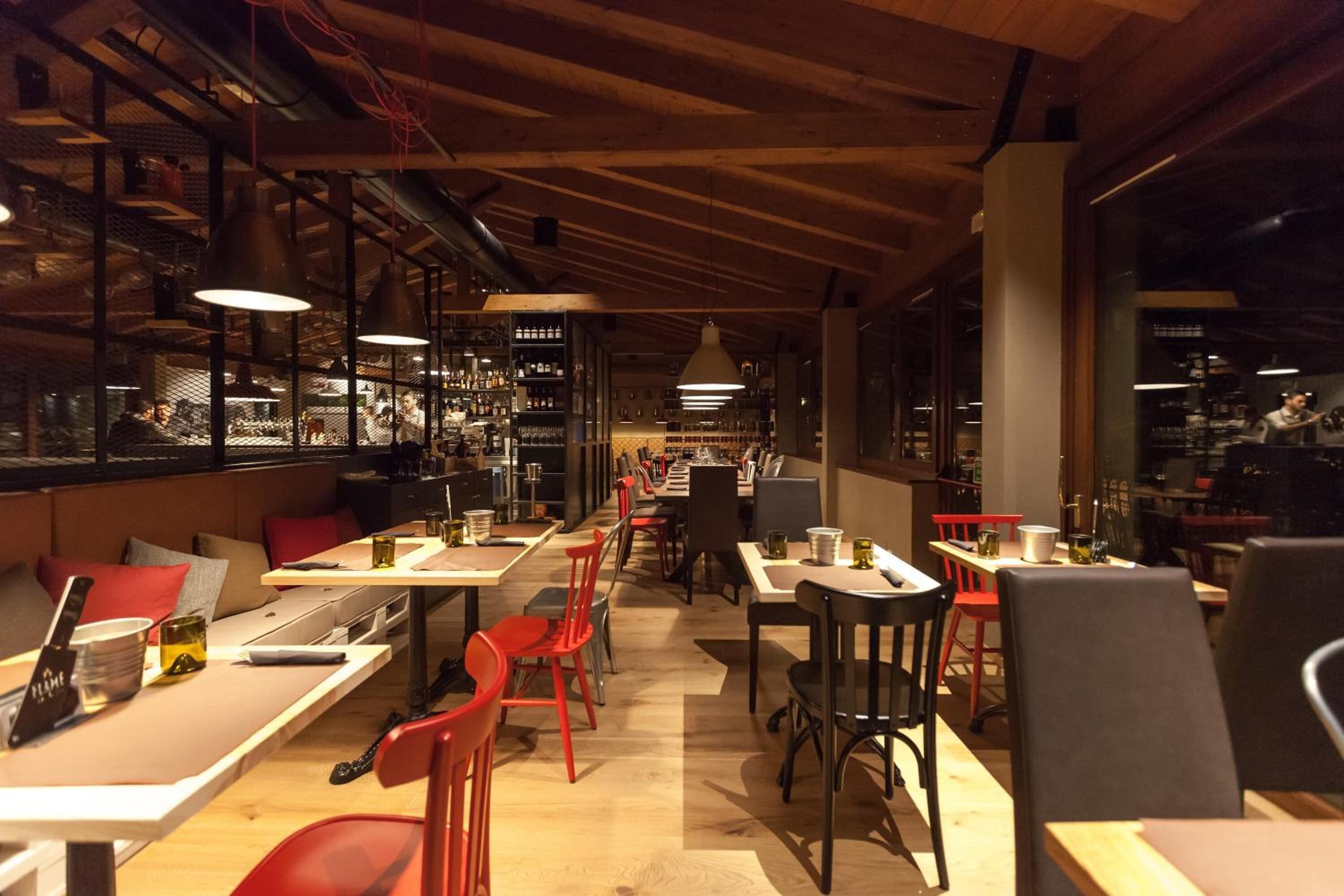 A restaurant with wooden ceiling beams, tables with red chairs, and shelves stocked with bottles.