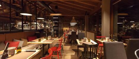 A restaurant with wooden ceiling beams, tables with red chairs, and shelves stocked with bottles.