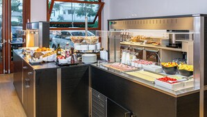 Un buffet proposant une variété de plats et de boissons, une machine à café et une vue sur l’extérieur par une fenêtre.
