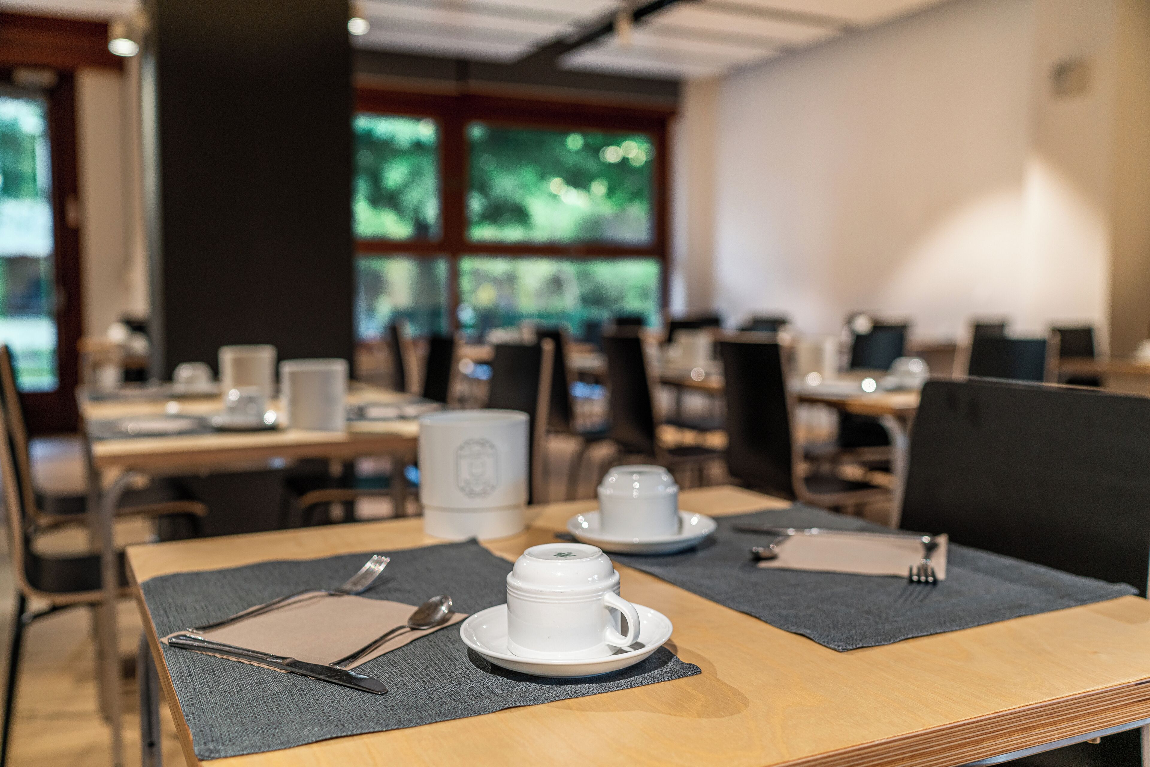 A dining area with tables set for breakfast, including cups and cutlery.