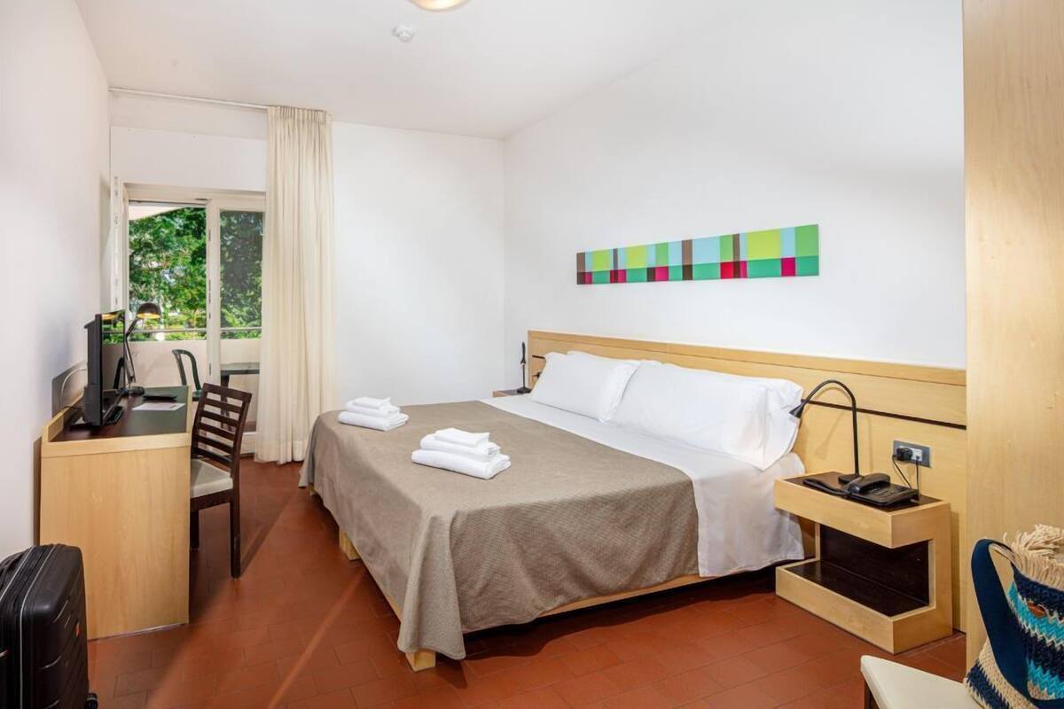Een hotelkamer met een bed, bureau, stoel en uitzicht op groen.