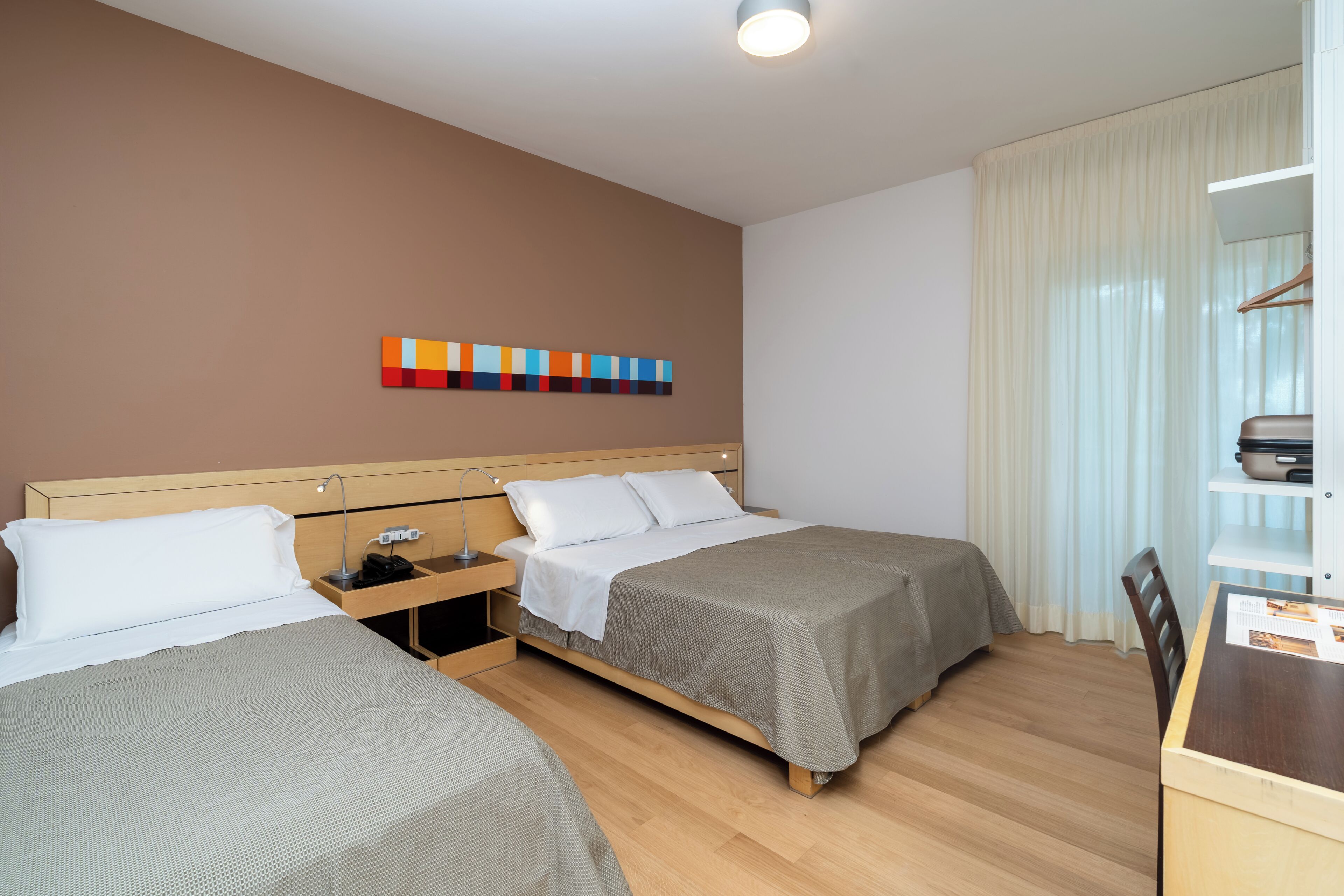 A hotel room with two beds, a desk, and a chair.