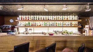 Un coin bar avec des chaises en bois, une horloge et des étagères remplies de bouteilles d’alcool.