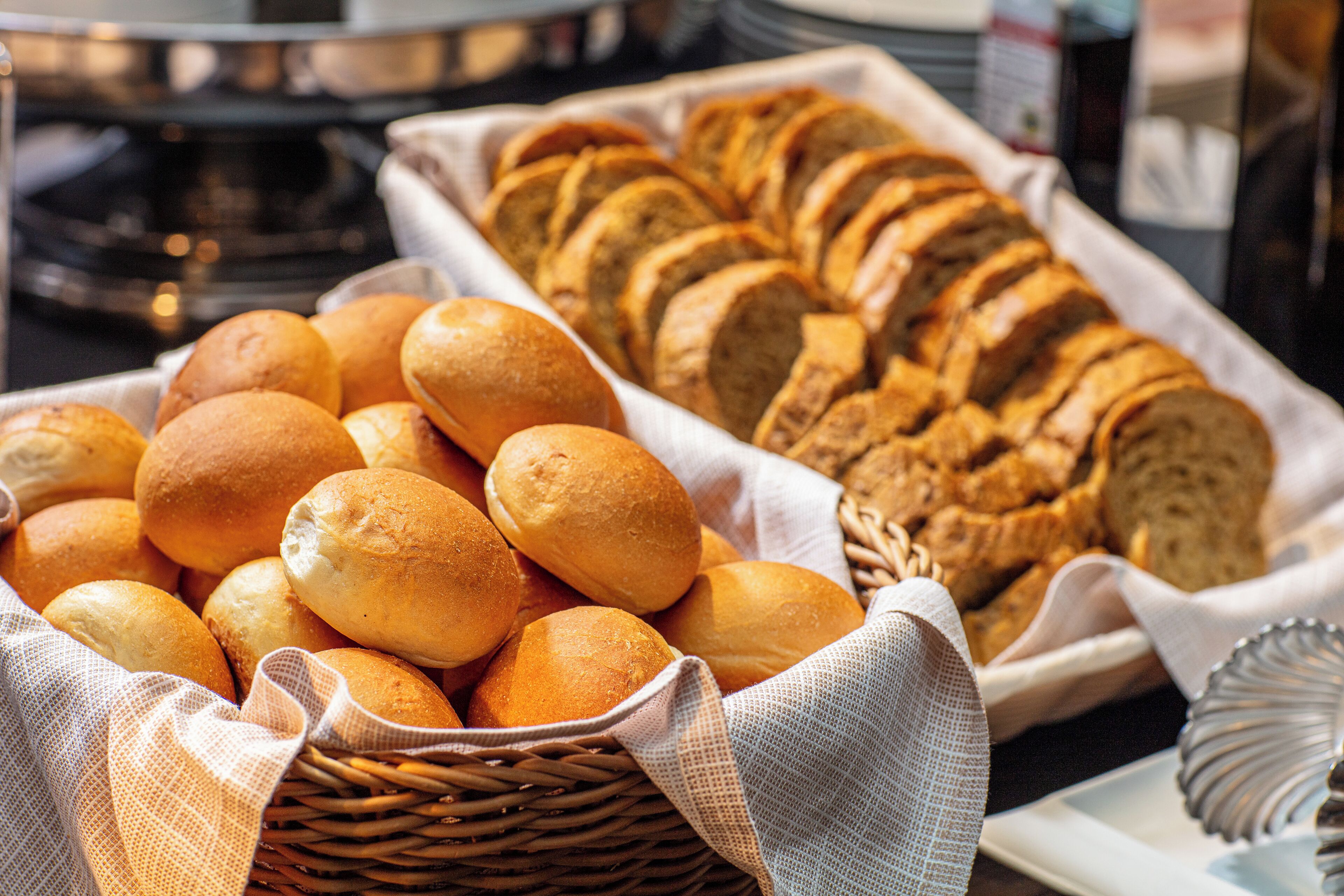 Een mand met versgebakken broodjes en sneetjes stokbrood op een tafel.