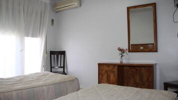 Una habitación con dos camas, un aparador de madera, un espejo y una ventana con cortinas.