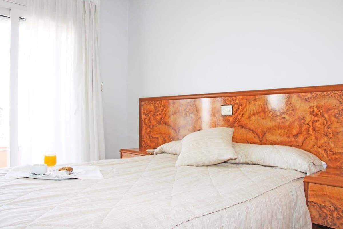 A neatly made bed with a wooden headboard, a bedside table with a lamp, and a breakfast tray with a glass of orange juice.