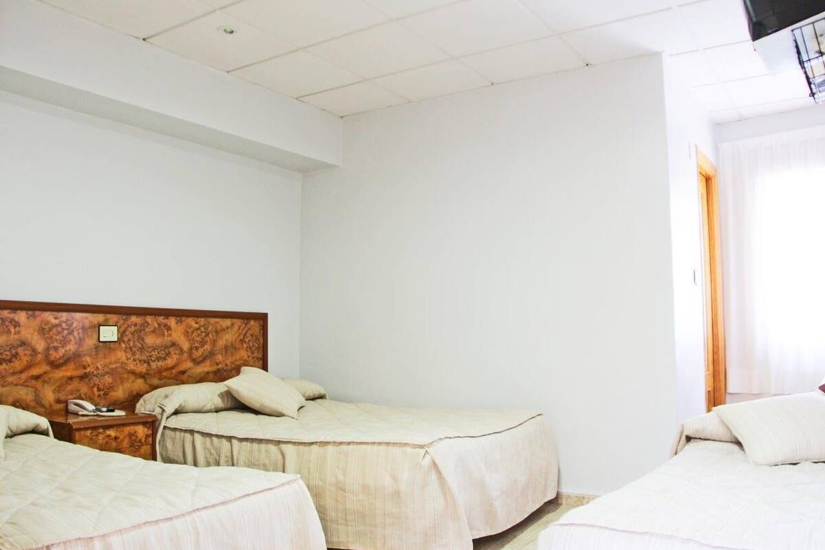 A hotel room with two single beds, a wooden headboard, a bedside table with a phone, and a window with curtains.