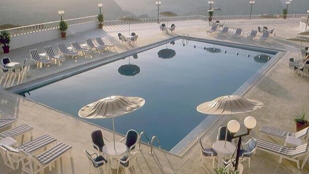 Piscina en la azotea con sillas de descanso y sombrillas, rodeada de montañas.