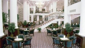 Un lobby espacioso con una escalera central, varias zonas de estar y un piso con diseño.
