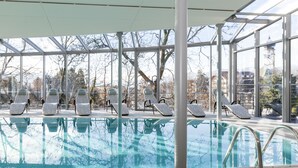A swimming pool with lounge chairs and a glass-enclosed area with a view of trees and buildings. - Hotel Heubad (Fie allo Sciliar)