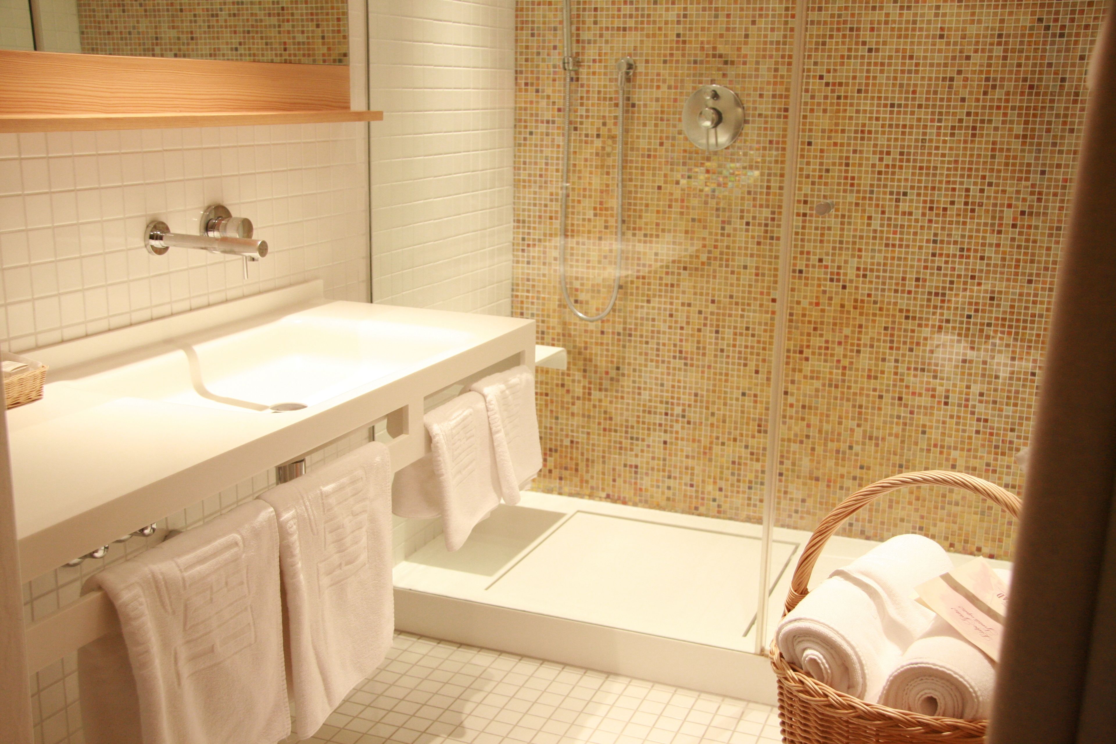 A bathroom with a white sink, a glass shower enclosure, and a wicker basket with towels.