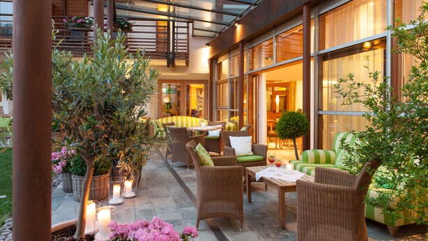 An outdoor seating area with wicker furniture, potted plants, and candles. - Hotel Heubad (Fie allo Sciliar)