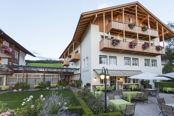 Un immeuble de deux étages abritant un café-restaurant au rez-de-chaussée et un balcon agrémenté de jardinières fleuries.