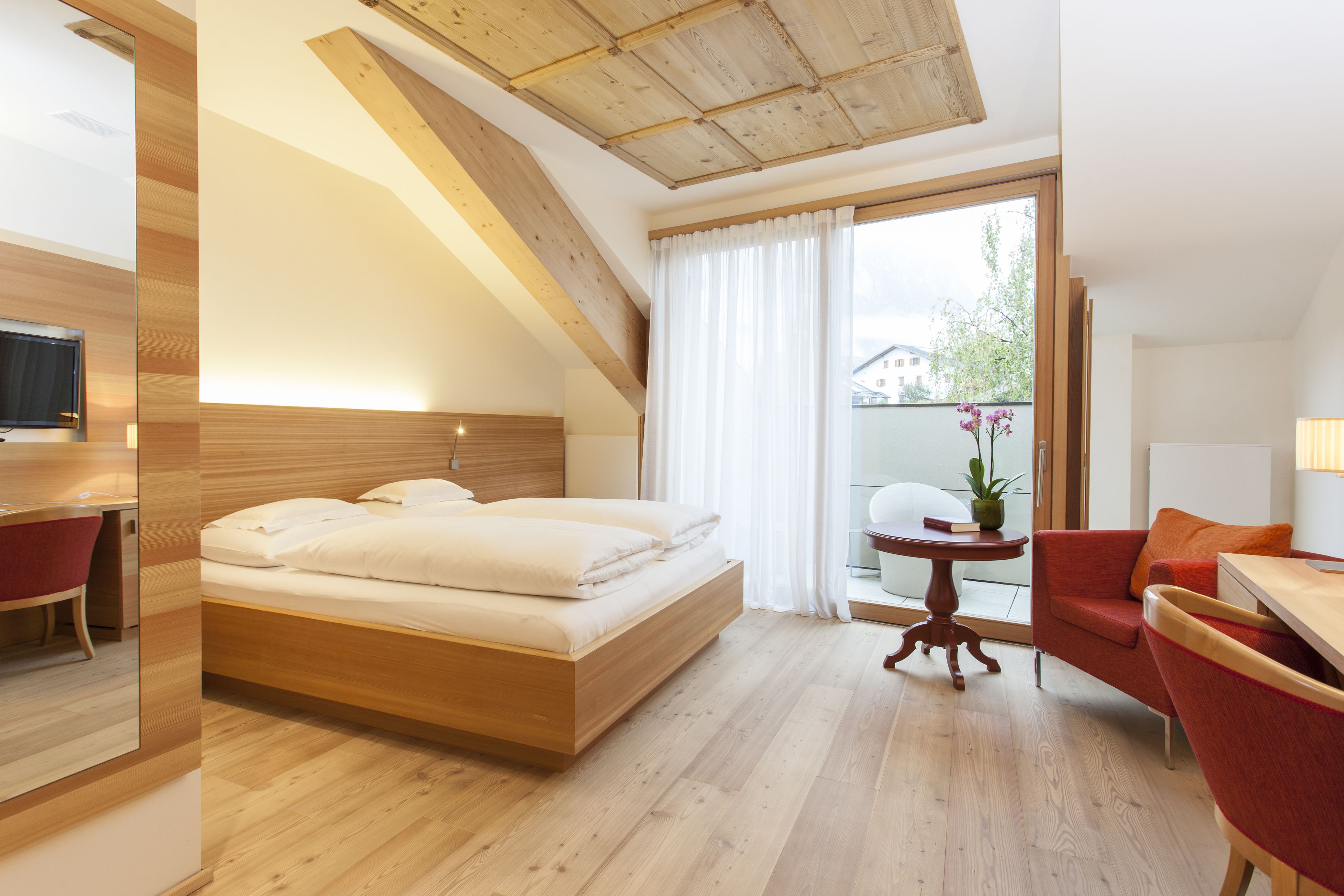 A modern bedroom with a wooden bed, a desk, a chair, and a small table with a plant.