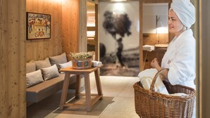 A spa room with wooden walls, a massage table, a massage therapist, and a wall-mounted massage machine. - Hotel Heubad (Fie allo Sciliar)
