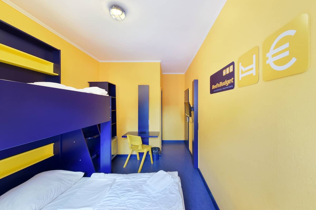 A hotel room with bunk beds, a desk, and a chair. There are signs on the wall indicating the room type and amenities.