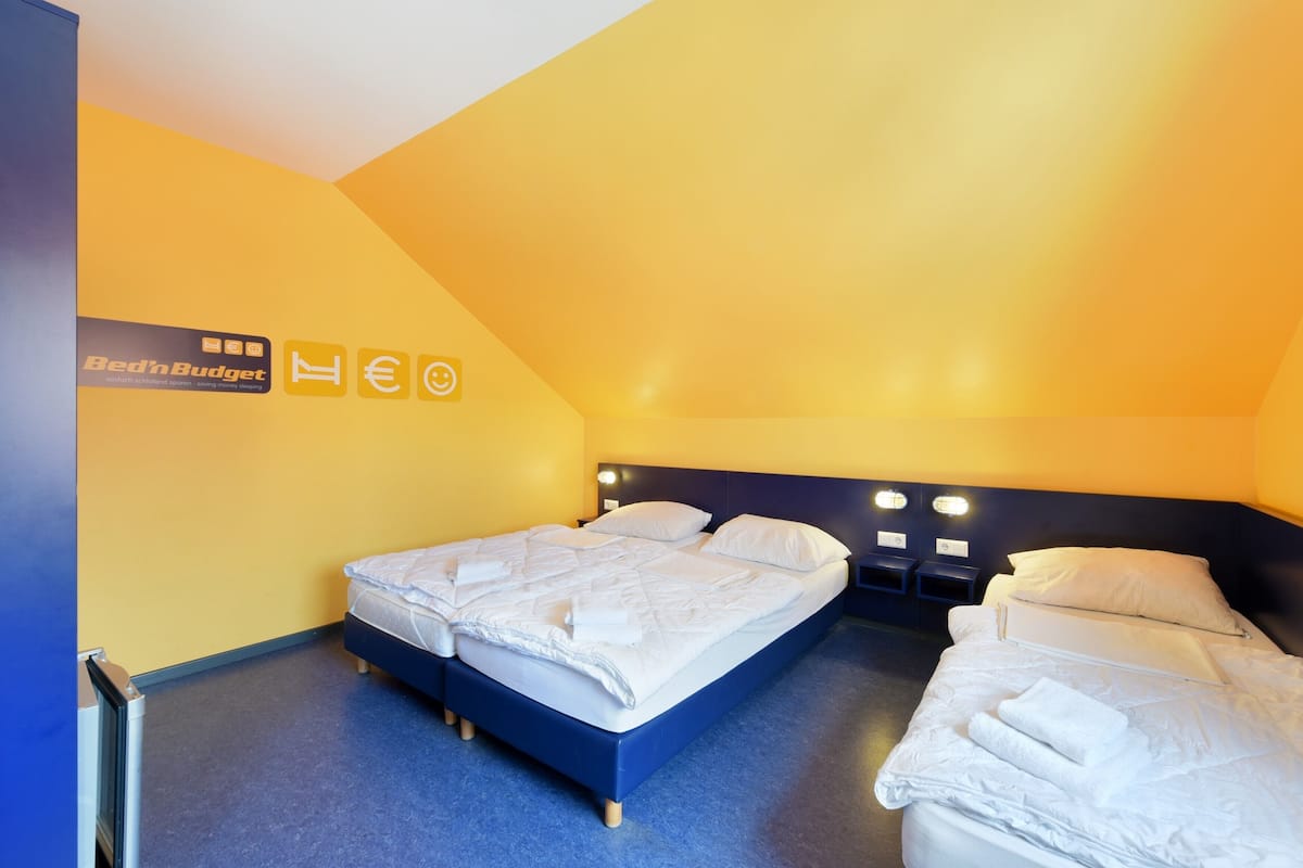 A room with two beds, a yellow accent wall, and a sign reading "Bed'n Budget."