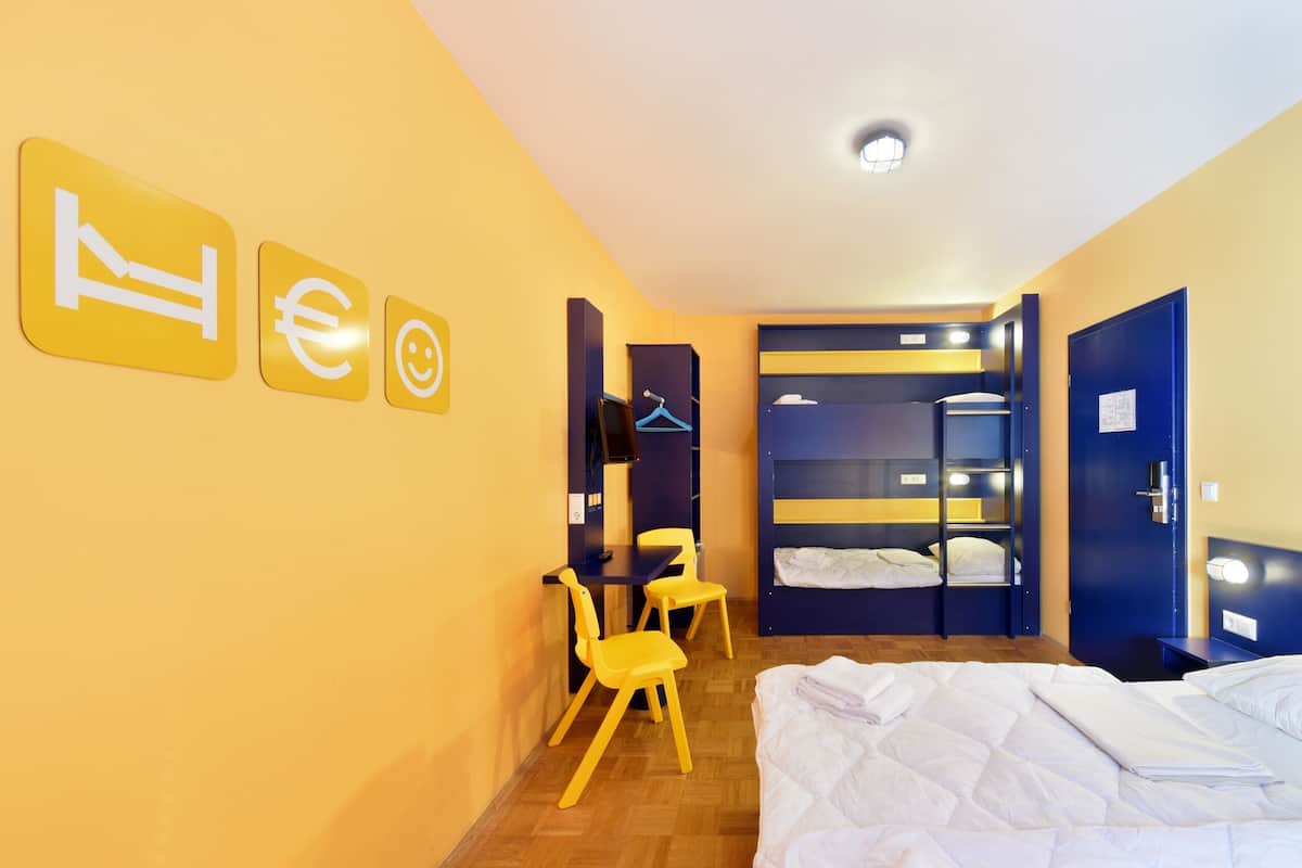 A hotel room with a bed, a desk, two chairs, a wardrobe, and a wardrobe with a mirror.