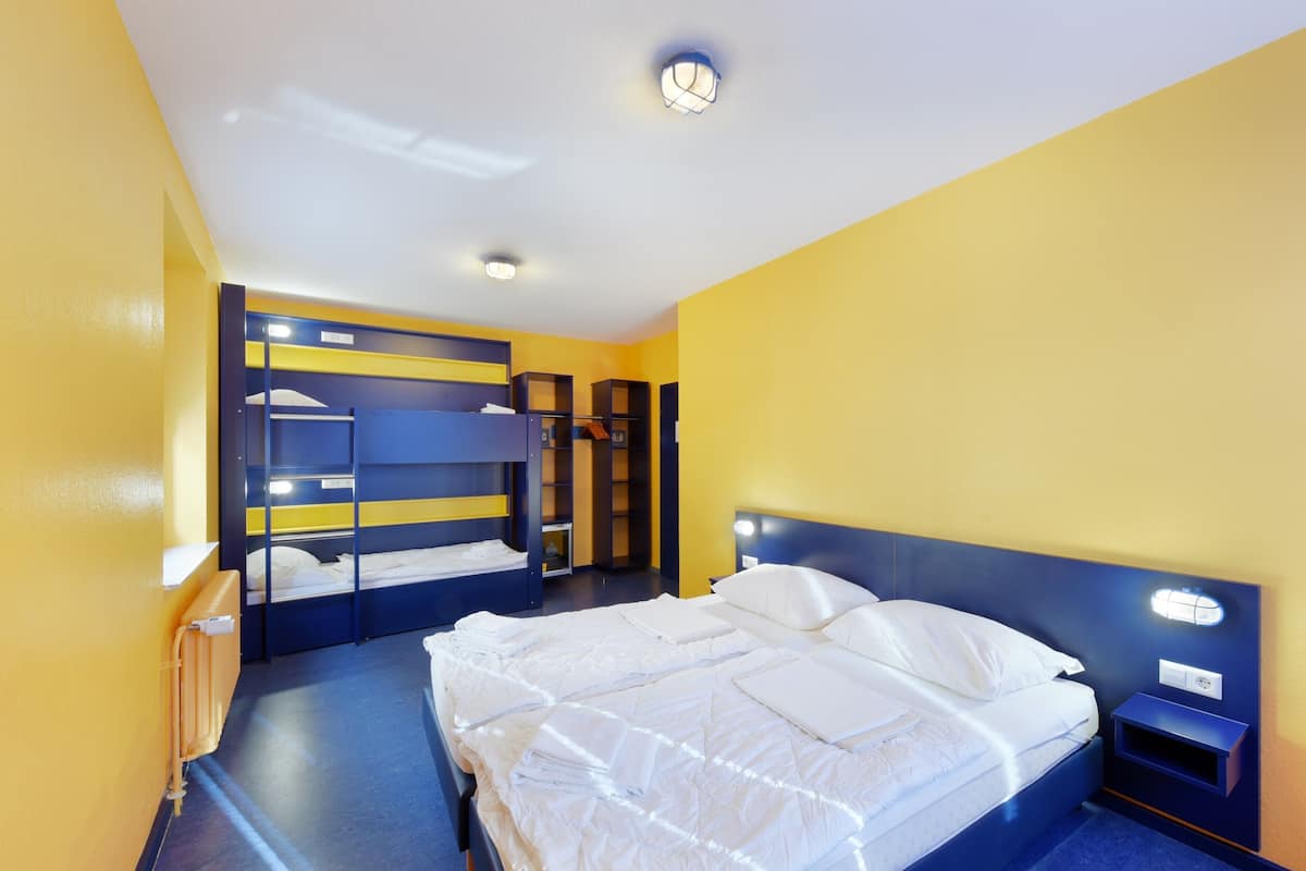 A hotel room with a bunk bed, a single bed, a nightstand, and a built-in wardrobe.