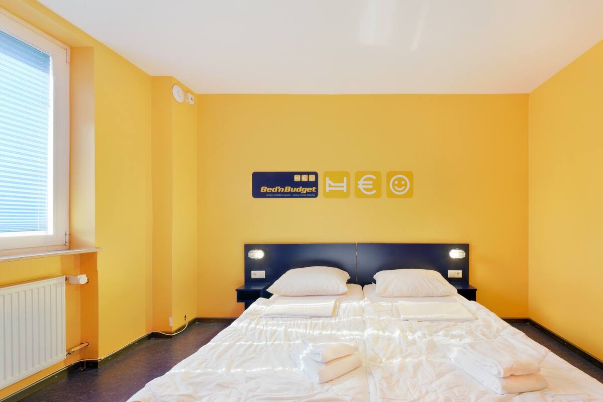 A hotel room with a yellow wall, a bed with white bedding, a nightstand, and a sign above the bed.