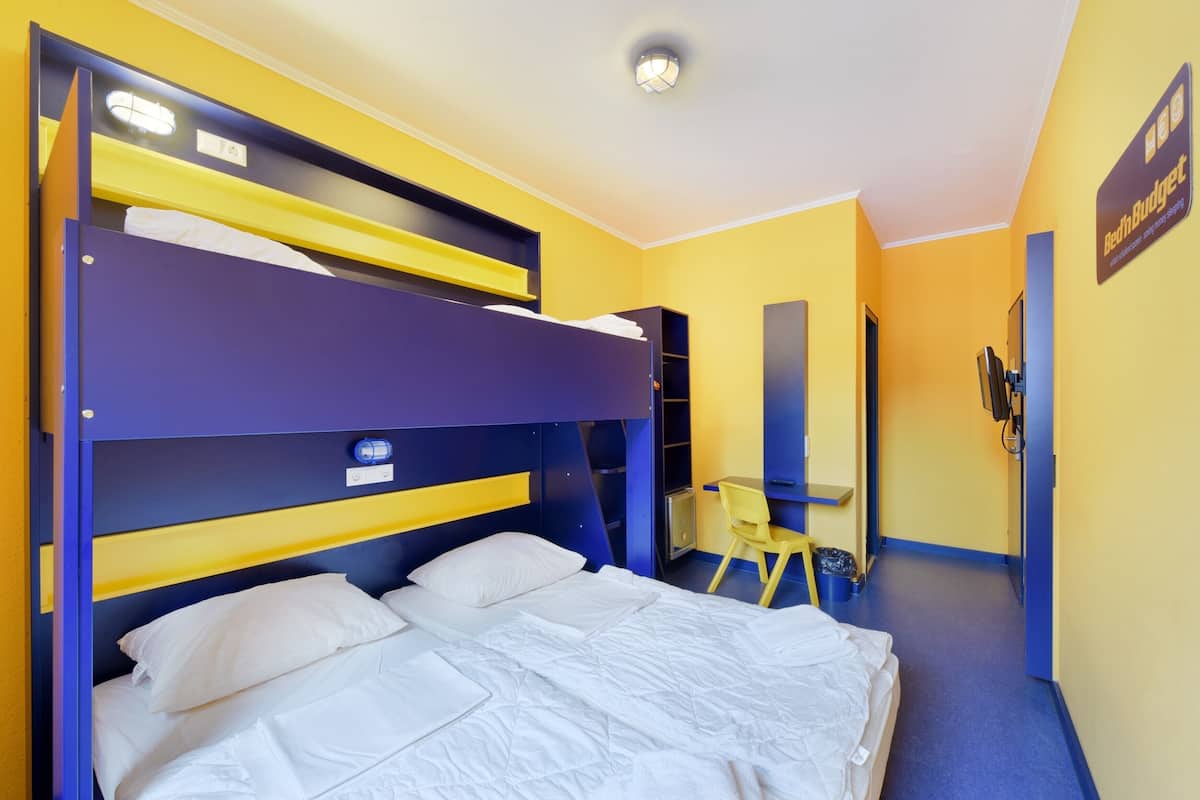 A bunk bed room with a desk and chair, a small trash bin, and a sign on the wall.