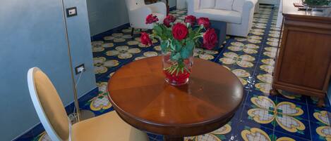 A dining area with a round wooden table, two white chairs, and a vase of red roses. The room has blue walls and a patterned floor.