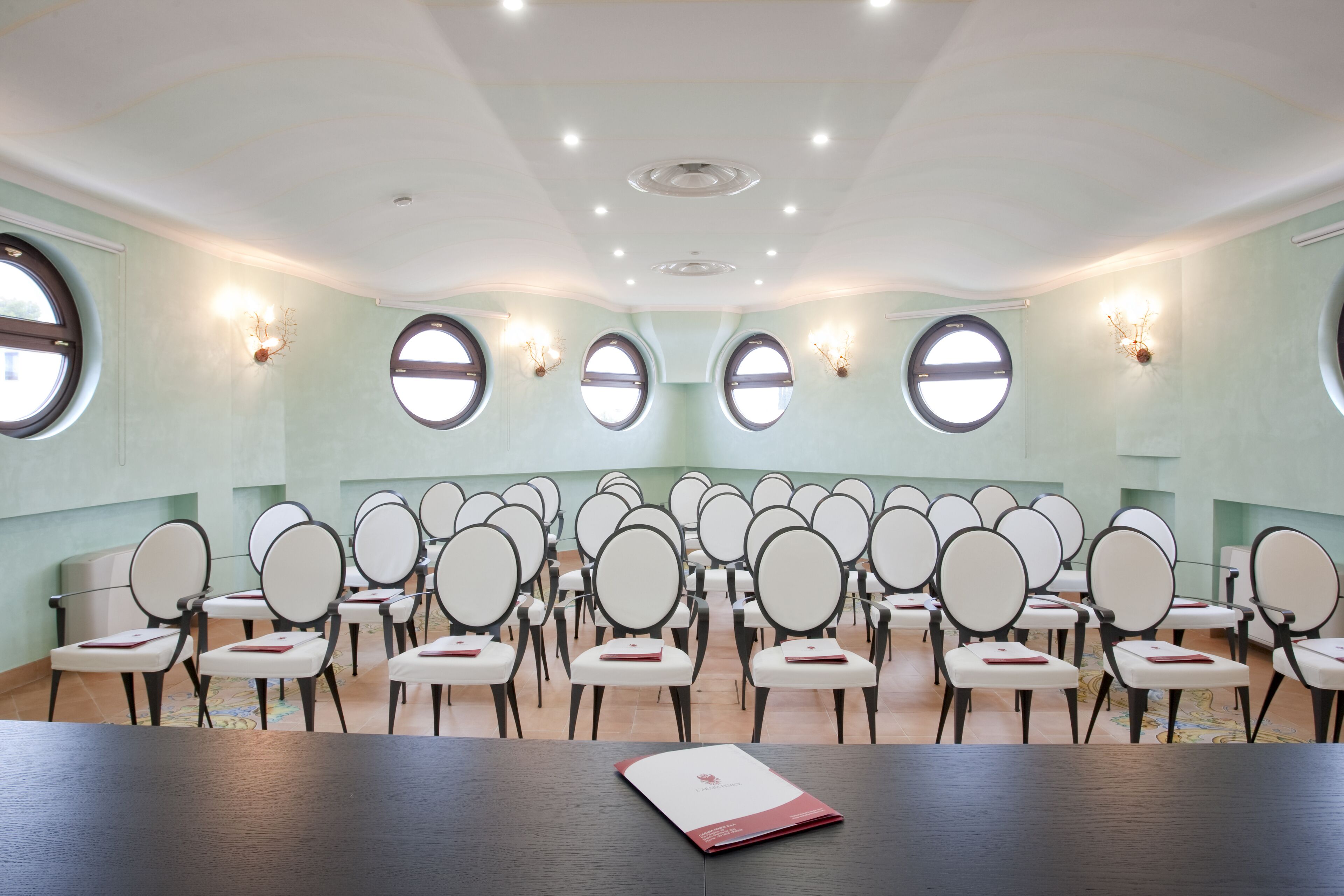 Un salón de conferencias con una larga mesa y numerosas sillas dispuestas en filas.