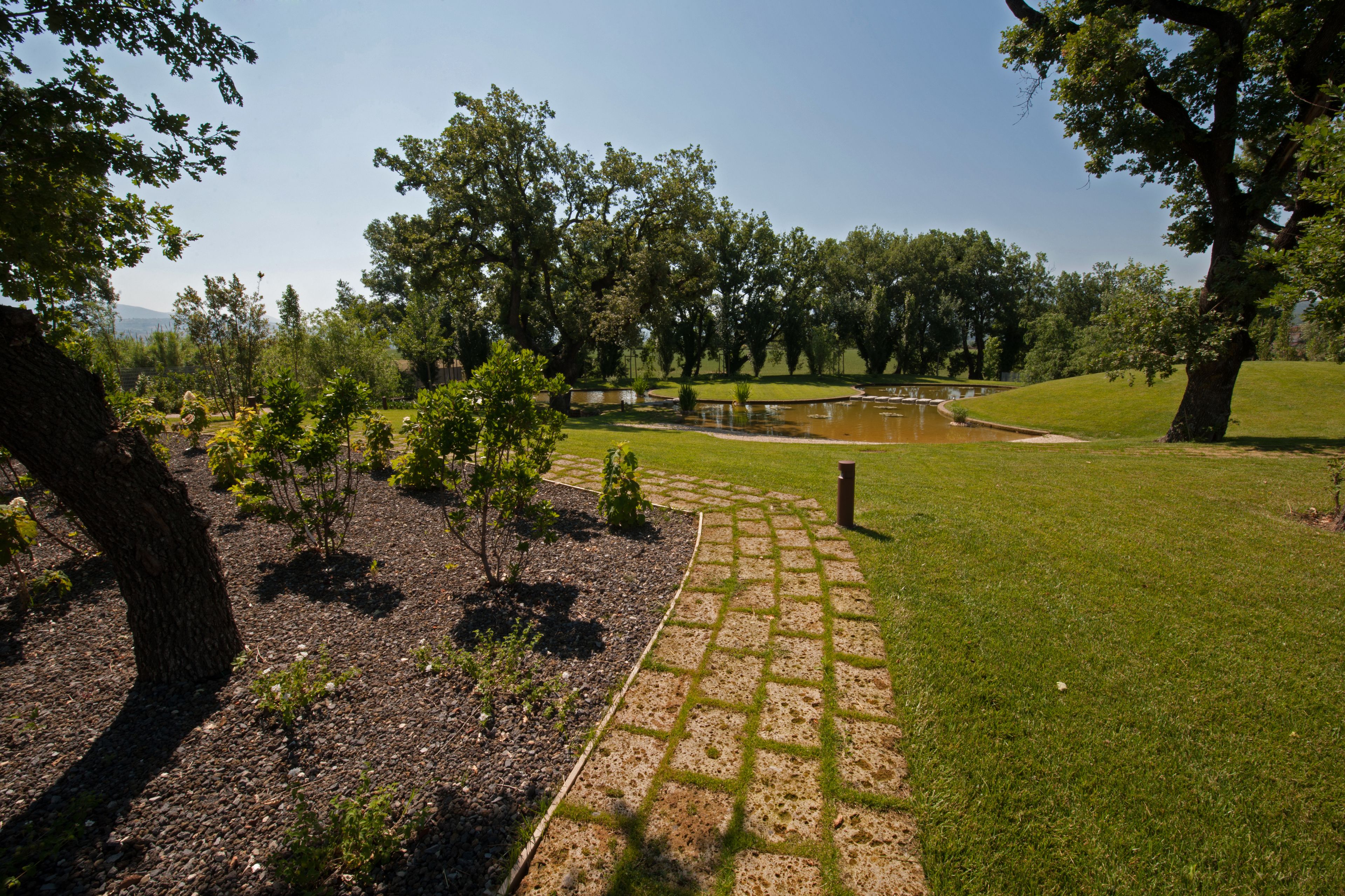 Un jardín ajardinado con un sendero empedrado, árboles y un estanque.