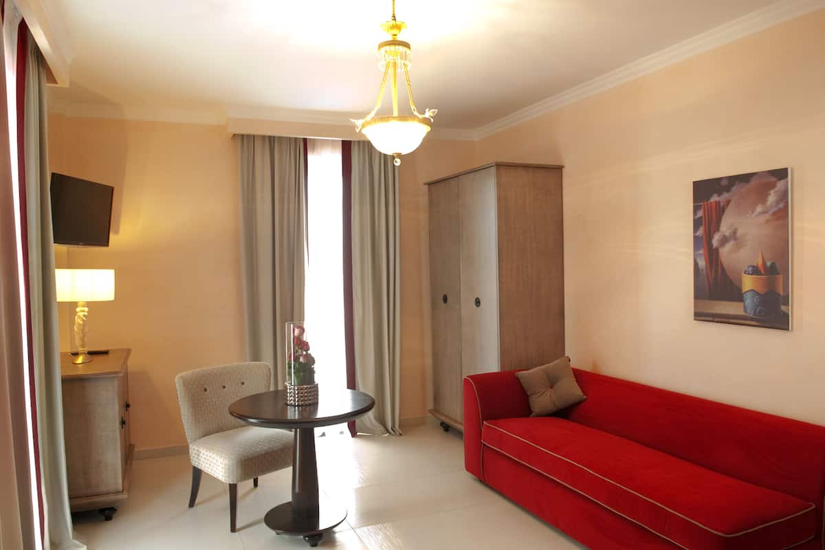 A hotel room with a red sofa, a round table with a vase of flowers, a television on the wall, and a wardrobe.