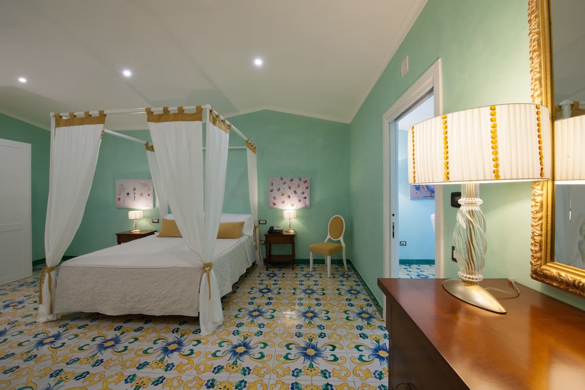 A bedroom with a four-poster bed, a chair, a bedside table, a lamp, and a mirror.