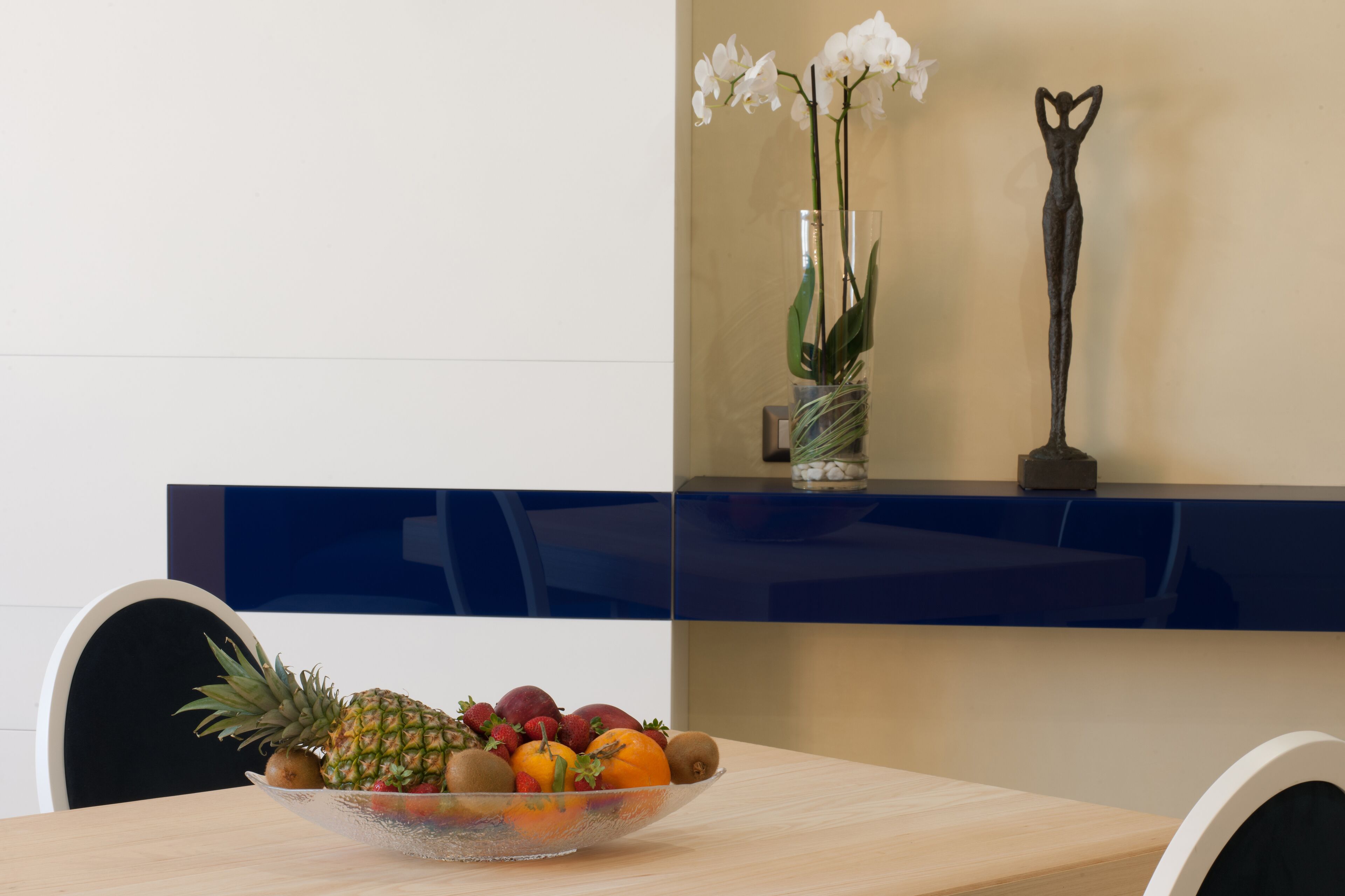 Ein Esstisch mit Obstschale, einer Vase mit weißen Blumen und einer Skulptur.