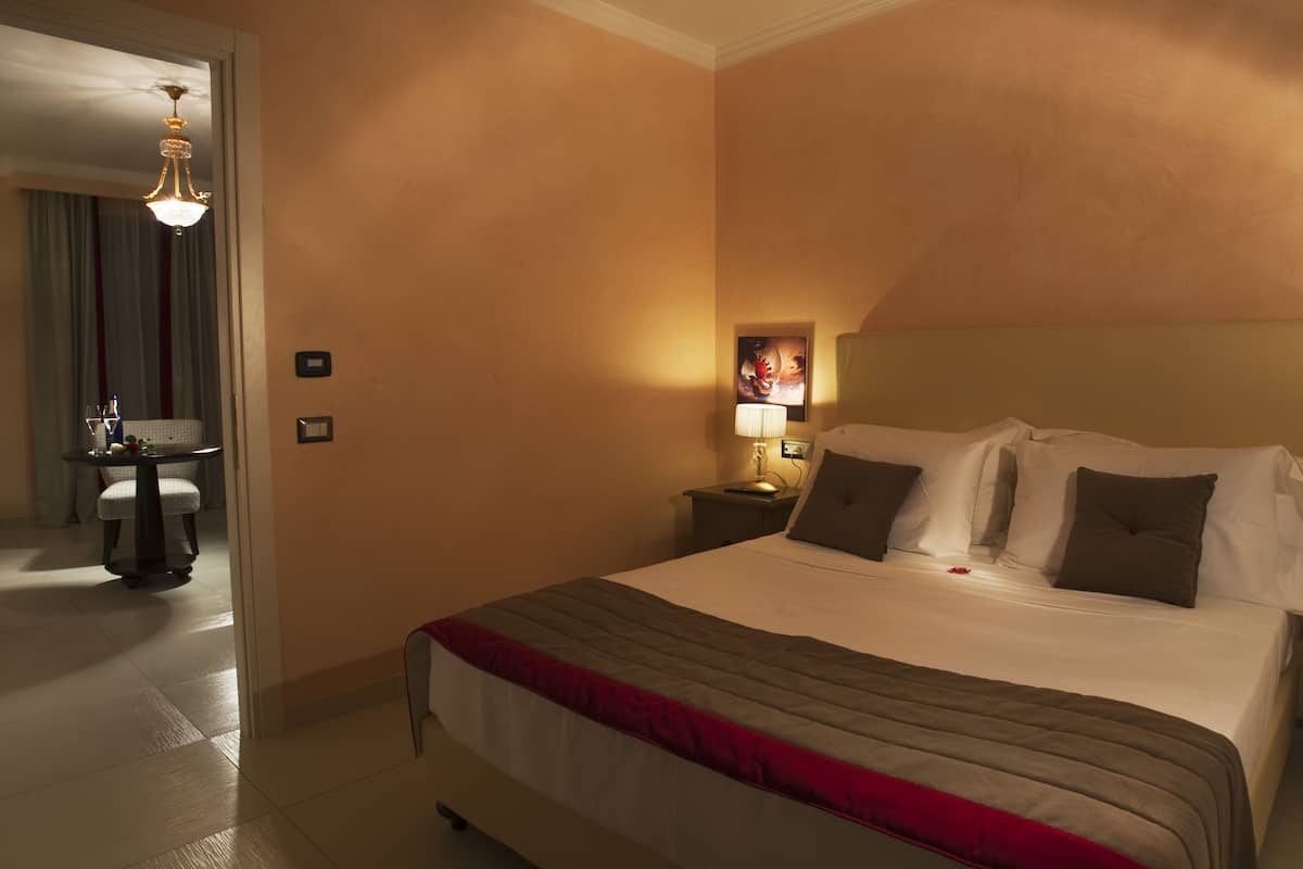 A hotel room with a large bed, a bedside table with a lamp, a painting on the wall, and a view of the bathroom.
