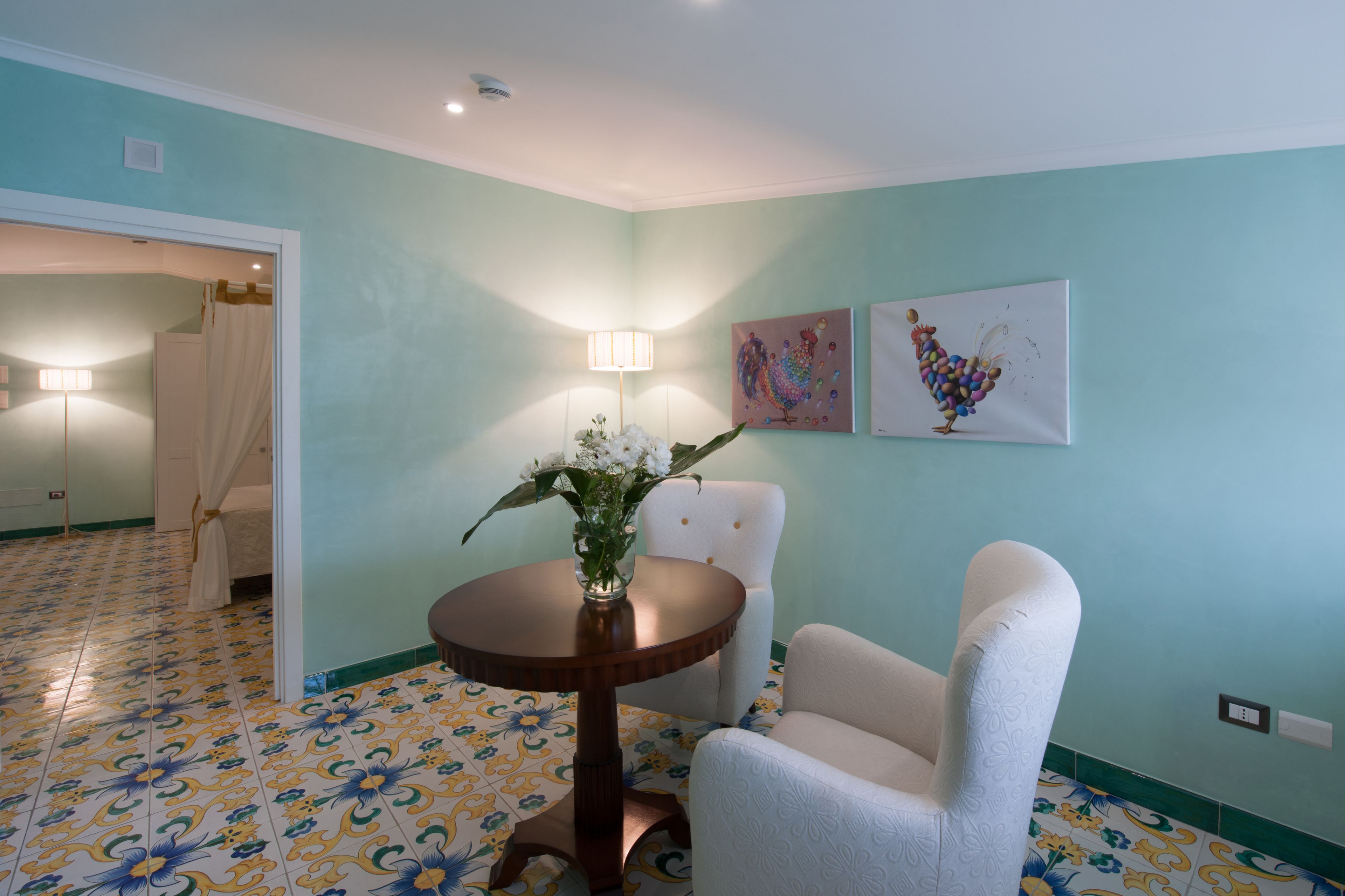 A room with a round wooden table, a white armchair, and two wall-mounted artworks.
