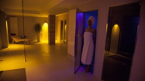 A spa area with a massage table, a potted plant, and a person in a towel near a glass door. - L'Araba Fenice (Altavilla Silentina)