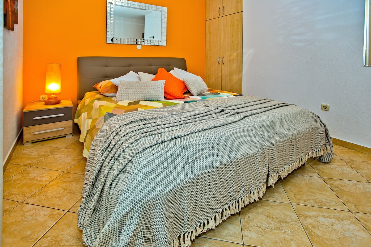 A bedroom with a bed, a nightstand, a lamp, a mirror, and a wardrobe.
