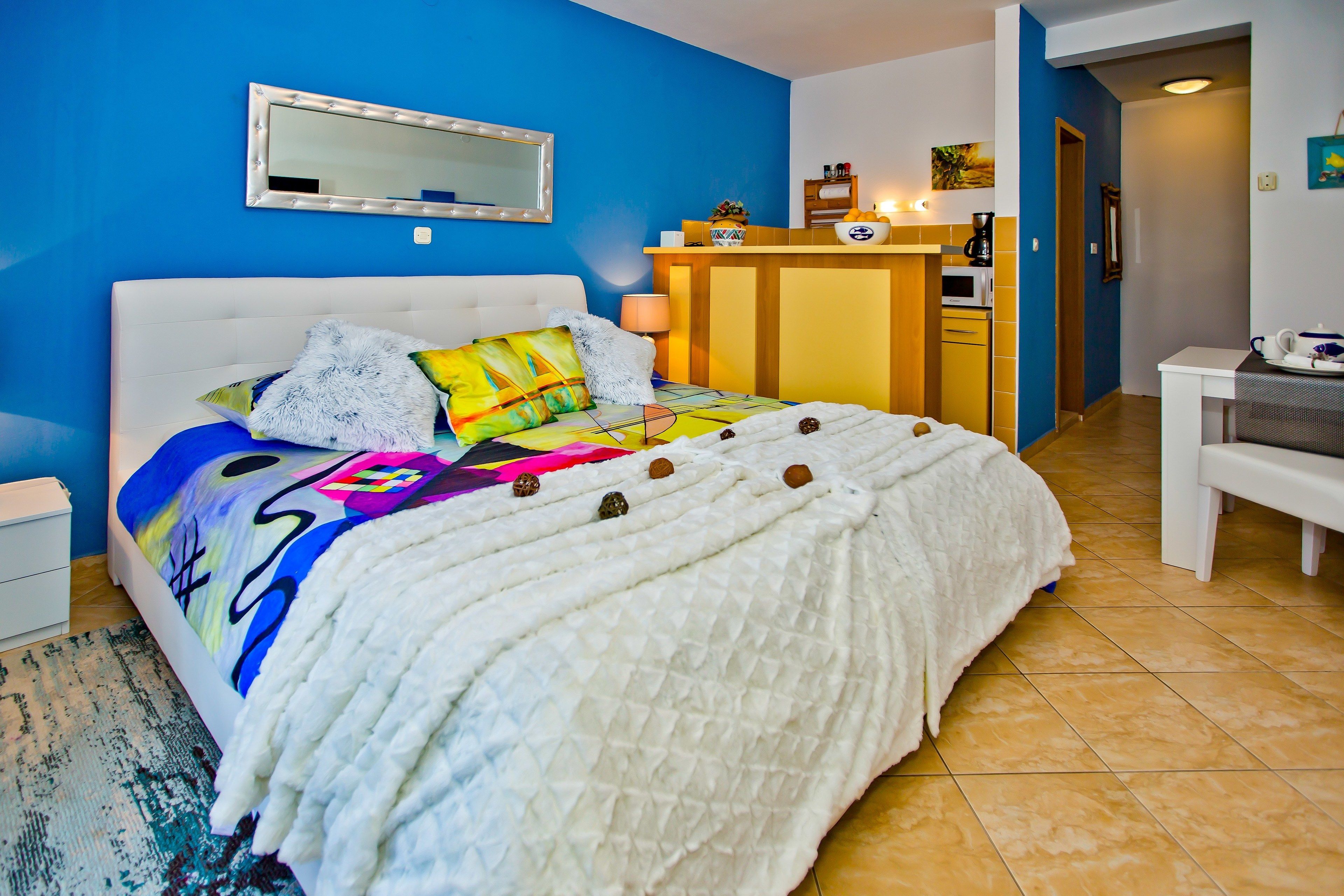 A bedroom with a bed, a bedside table, a mirror, a desk, and a chair.