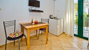 A small kitchenette with a TV, a coffee maker, and a refrigerator. There is a dining table with chairs and a colorful chair.